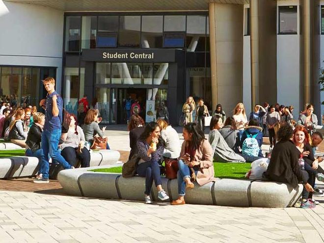 A sunny day in University square. Students are sat out on the blocks and the image point of view is looking at Student Central.